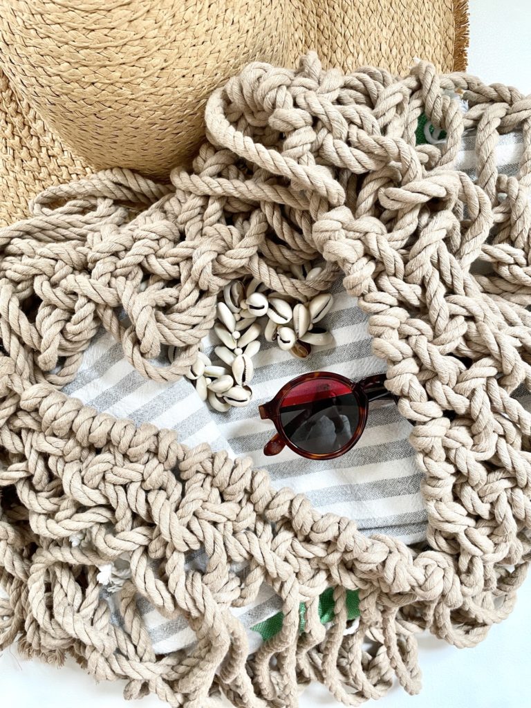 Macrame beach bag detail with sun glasses, hat and shells